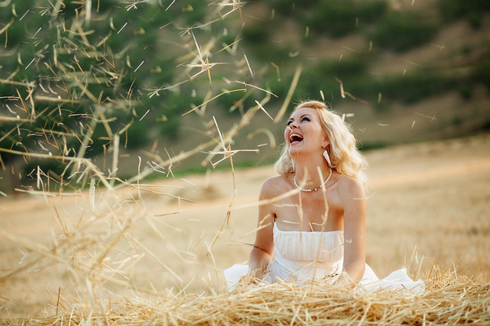 Happy bride playing with hey in field at her wedding day