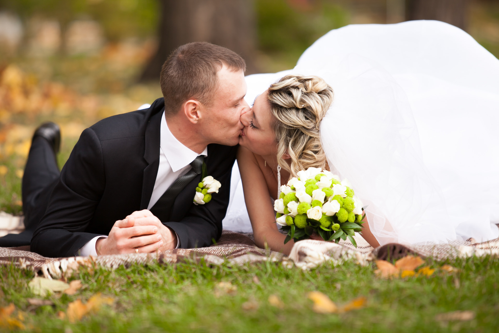 newly married couple lying on grass at park and kissing